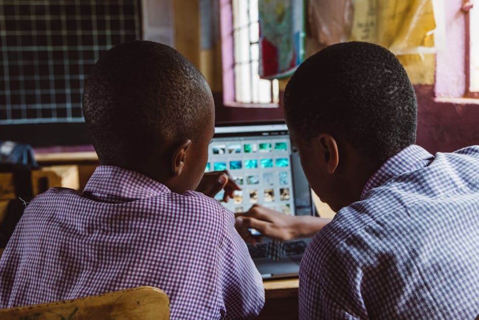 Two schoolchildren in uniform collaborate on a laptop in a classroom setting, focused on learning.